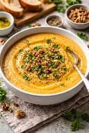 طريقة-عمل-شوربة كريمة القرنبيط والجزر المشوي في وعاء أبيض كبير مع لمسة من البقدونس الطازج وزيت الزيتون والفلفل الأسود