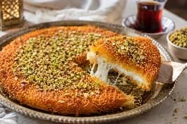 طريقة-عمل-صينية كنافة مصرية ذهبية ومقرمشة محشوة بالجبنة والمكسرات، يعلوها القطر اللامع وقطع الفستق، تقدم في طبق كبير مع الشاي