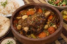 طريقة-عمل-طاجن فخار مصري تتصاعد منه الأبخرة، به موزة ضاني طرية بالثوم والجزر والبصل، تقدم مع أرز بالشعرية وخبز بلدي