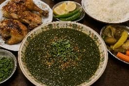 طريقة-عمل-طبق ملوخية خضراء مخملية القوام تعلوها زفرة الثوم والكزبرة الذهبية، بجانب أرز أبيض مفلفل وقطع دجاج بلدي مشوي، في مشهد يعكس أصالة السفرة المصرية
