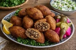 طبق كبة عراقية مقلية ذهبية ومقرمشة، كرات بيضاوية الشكل محشوة بلحم مفروم متبل بالبهارات، الصنوبر، والجوز، تقدم على طبق تراثي مع شرائح الليمون، البقدونس الطازج، والمخللات، إلى جانب سلطة الزبادي والخيار