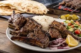 طبق ريش غنم عراقية مشوية على الفحم بالبهارات السبعة والثوم، أضلاع ذهبية مقرمشة متبلة بتتبيلة طويلة مع الفحم المشتعل والدخان، تقدم مع أرز بسمتي أبيض وسلطة وليمون