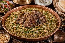 طبق فريكة أردني فاخر، حبوب فريكة خضراء مدخنة مفلفلة مع قطع لحم ضأن ذائبة وصنوبر محمص ولوز، مزين بالبقدونس الطازج في صينية تقديم نحاسية على مائدة أردنية تقليدية