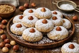طريقة-عمل-كحك العيد المحشو بالبندق المحمص، مرشوش بالسكر البودرة، مع حبات بندق كاملة على الوجه وأوراق بندق خضراء