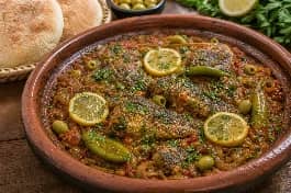 طاجن قلاية سمك مغربي بصلصة الطماطم والبصل والفلفل الحار والكزبرة، مع قطع السمك الذهبية وشرائح الليمون والخبز المغربي