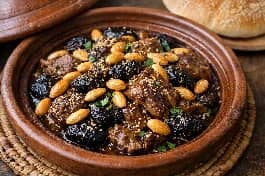طريقة-عمل-طاجين مغربي تقليدي باللحم والبرقوق واللوز المحمص مع رشة سمسم، يقدم في طبق طاجين فخاري