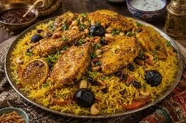 طبق مقلوبة سمك عماني ذهبي يظهر طبقات الأرز البسمتي المفلفل وقطع السمك المقلي المتماسك، مزين باللومي واللوز والصنوبر والبقدونس