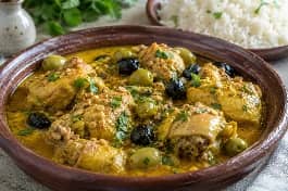 طريقة-عمل-طاجن دجاج صومالي بالزعفران والزيتون في صلصة كريمية ذهبية، قطع دجاج طريّة وزيتون أخضر وأسود في طبق فخاري مع الأرز البسمتي