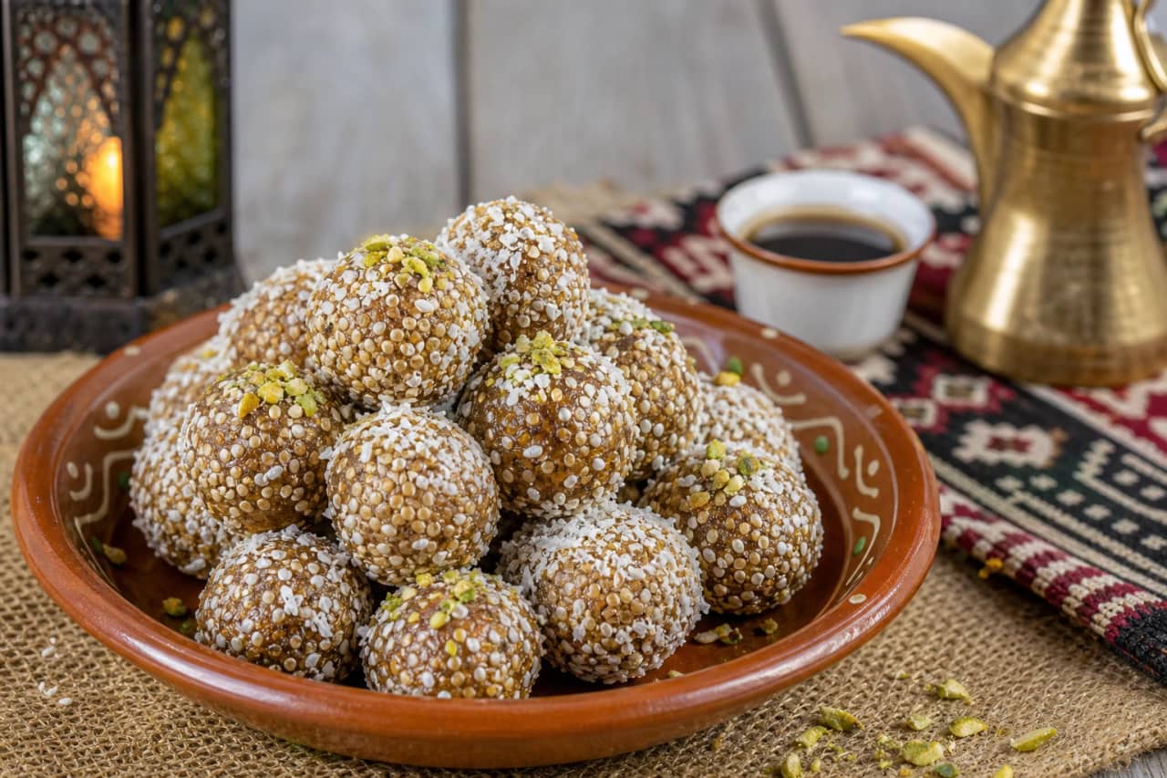 كرات حلوى التمر الهندي البحرينية متماسكة وذهبية مغطاة بالسمسم وجوز الهند، تقدم في طبق فخاري صغير مع قهوة عربية