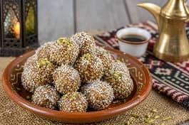 كرات حلوى التمر الهندي البحرينية متماسكة وذهبية مغطاة بالسمسم وجوز الهند، تقدم في طبق فخاري صغير مع قهوة عربية