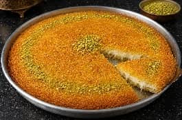 كنافة سادة ذهبية مقرمشة في صينية دائرية مع قطر ساخن وفستق حلبي مطحون على الوجه