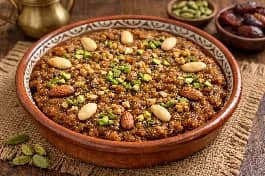 طريقة-عمل-طبق حيسة سعودية تقليدية بالتمر والمكسرات في صحن تقديم فخاري مزين بالهيل والمكسرات