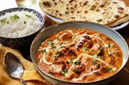 طبق دجاج ماسالا بريطاني كريمي برتقالي ذهبي، قطع دجاج تندوري مشوية تسبح في صلصة الطماطم والكريمة الغنية بالبهارات، مزين بالكريمة الطازجة والكزبرة الخضراء، مع أرز بسمتي وخبز نان بالثوم على طاولة أنيقة