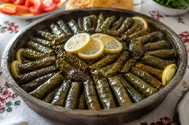 طبق محشي ورق عنب مصري، أصابع ورق عنب خضراء لامعة بزيت الزيتون، محشوة بالأرز والأعشاب، مرصوصة بشكل دائري في قدر، مع شرائح الليمون الصفراء على الوجه، على مائدة مصرية تقليدية
