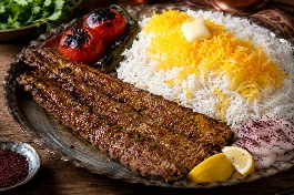 سيخ كباب كوبيده إيراني طويل ذهبي مشوي على الفحم، لحم خروف مفروم معطر بالزعفران والبصل، مقدم على أرز بسمتي أبيض مفلفل مع الزعفران، طماطم مشوية، وفلفل حار، وقطعة زبدة على الأرز