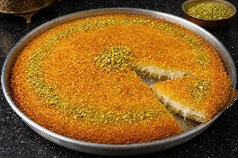 كنافة سادة ذهبية مقرمشة في صينية دائرية مع قطر ساخن وفستق حلبي مطحون على الوجه