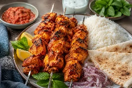 طبق دجاج تكا كويتي بالزبادي والبهارات الحارة، قطع دجاج ذهبية اللون ومتفحمة الأطراف على أسياخ، تقدم مع أرز أبيض وخبز تنور وليمون ونعناع طازج