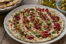 طبق بابا غنوج فلسطيني بالرمان والجوز المدخن، باذنجان مشوي ومتبل بالطحينة والليمون، مزين بحب الرمان الياقوتي والجوز المحمص وزيت الزيتون، مع خبز عربي محمص على الجانب