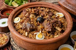 طبق رز حساوي سعودي في قدر فخاري، أرز بني مدخن مفلفل مع قطع لحم ضأن متبلة بالبهارات الخليجية واللومي، مزين بالمكسرات والزبيب على مائدة تراثية أحسائية