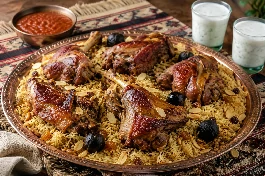 طبق تقديم نحاسي كبير يحمل كبسة لحم سعودية ذهبية اللون، يتصدره قطع لحم غنم طرية بالعظم بلون محمر لامع، الأرز البسمتي طويل الحبة مفلفل ومتبل بالزعفران والهيل والقرنفل، مزين باللوز المحمص والزبيب الذهبي وشرائح الليمون المجفف (لومي)، على مفرش عربي تقليدي بجانب طبق سلطة الدقوس الحارة وكاسات اللبن