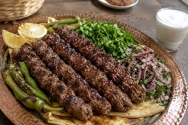 طبق نحاسي كبير يحمل أسياخ كباب حلبي سورية مشوية على الفحم، قطع اللحم المفروم بخشونة والمتبلة بالبهارات الحلبية تتخللها بقع سوداء من الفحم، تقدم فوق خبز عربي محمص، مزينة بجبل من البقدونس الطازج المفروم وشرائح البصل الأحمر السماقي وحلقات الفلفل الأخضر الحار، بجانب طبق من اللبن الرائب المثلج وشرائح الليمون