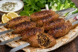 طريقة-عمل-أقراص كبة مشوية على الفحم الحجري بتوهج ذهبي محمر، محشوة باللحم المفروم والصنوبر والدهن، مقدمة على فرش من الخبز التنوري مع شرائح الليمون والنعناع الأخضر