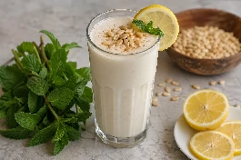 طريقة-عمل-كوب طويل من عصير اللب الأبيض الكريمي مزين بحبات اللب المحمص وشرائح الليمون، بجانبه باقة نعناع أخضر