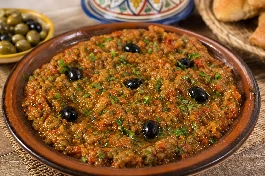 سلطة زعلوك مغربية باذنجان مدخن وطماطم متماسكة في طبق خزفي مع زيت الزيتون وكمون وكزبرة خضراء